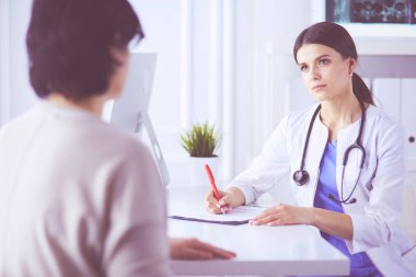 Doktor ve hasta hastane danışma odasında tıbbi sorunları tartışıyorlar. Doktor hasta formunu dolduruyor.