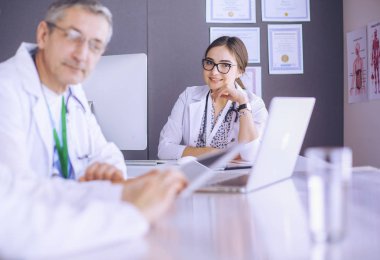 Ciddi bir tıbbi ekip parlak bir ofiste dizüstü bilgisayar kullanıyor.