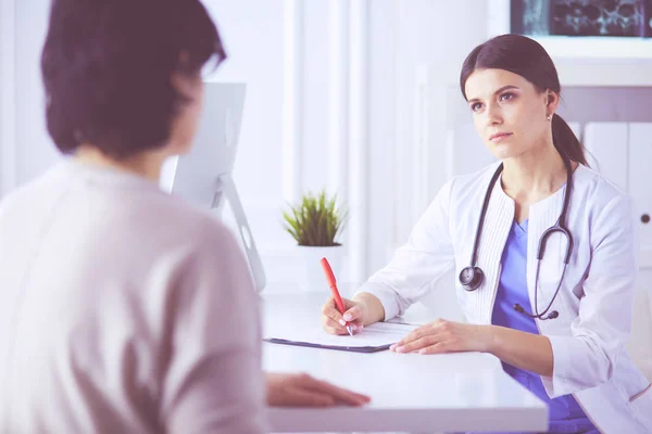 Médico y paciente discutiendo problemas médicos en una sala de consulta del hospital. Doc rellenando un formulario de pacientes — Foto de Stock