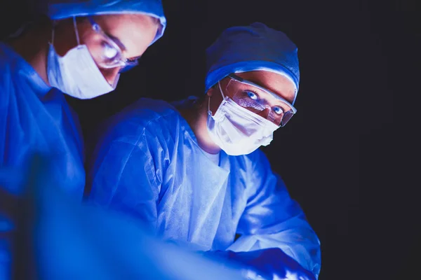 Equipe de médicos em cirurgia em um fundo escuro. — Fotografia de Stock