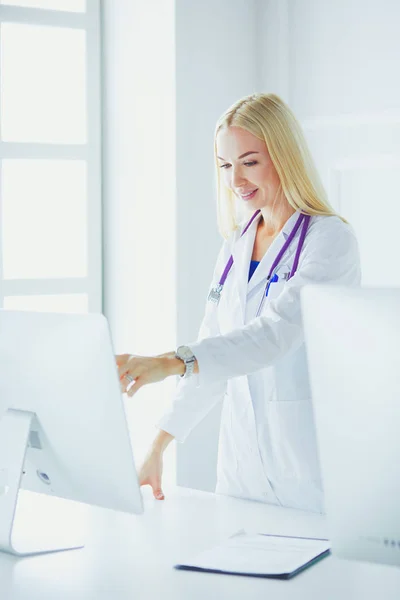 Fiatal nő orvos a munkahelyen, miközben a számítógép felé mutat a kórházi irodában.. — Stock Fotó