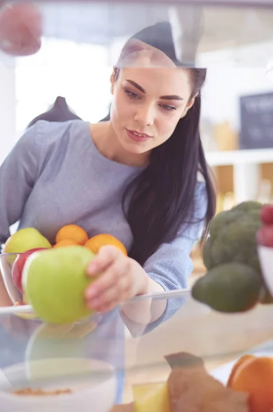Smiling woman taking a fresh fruit out of the fridge, healthy food concept — Stock Photo, Image