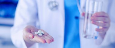 Doktorların ellerinde haplar ve bir bardak su tutarken yakın plan çekimleri..