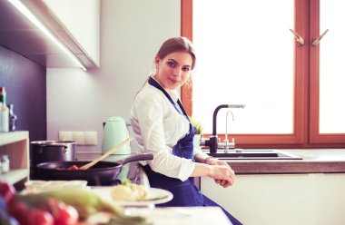 Mutfakta sobanın yanında duran genç bir kadın.