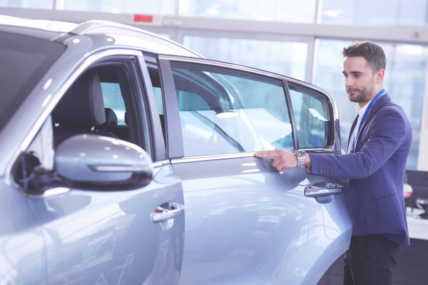 Дилер стоит рядом с новой машиной в выставочном зале
.