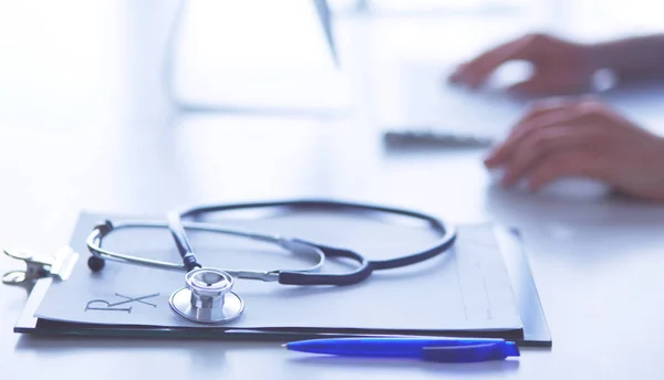 Primer plano del estetoscopio se encuentra en la mesa cerca del médico femenino escribiendo en el ordenador portátil — Foto de Stock