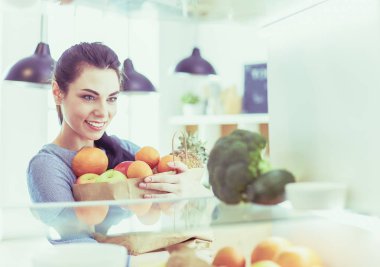 Gülümseyen kadın buzdolabından taze meyve alıyor, sağlıklı yiyecek konsepti.