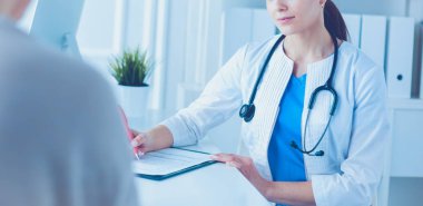 Doktor ve hasta hastane danışma odasında tıbbi sorunları tartışıyorlar. Doktor hasta formunu dolduruyor.