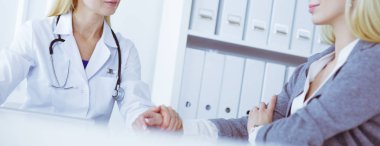 Hasta bir tıbbi Danışma alma ve kameraya bakarak gülen, kadın doktor masada oturuyor