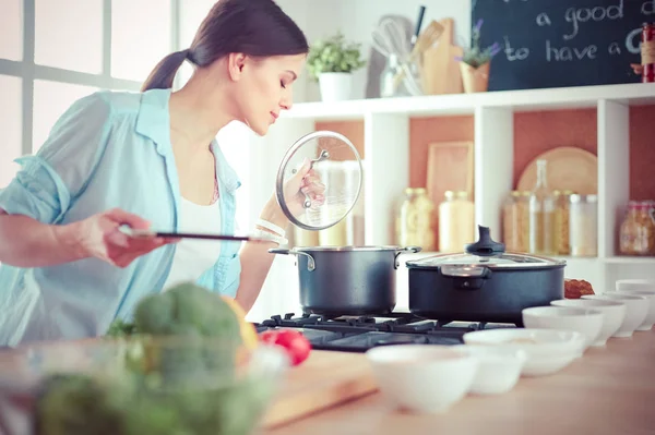 Jovem mulher em pé junto ao fogão na cozinha — Fotografia de Stock