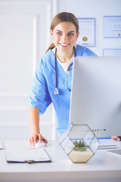 Mladý lékař žena stojící u stolu, izolované na bílém pozadí — Stock fotografie