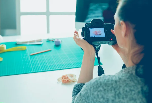 Mujer joven diseñadora de pie cerca del lugar de trabajo y fotografiándolo en una cámara digital — Foto de Stock