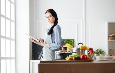 Mutfakta yemek yapmak için tablet bilgisayar kullanan genç bir kadın.