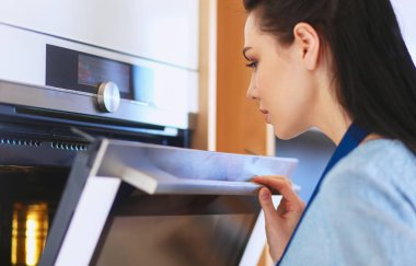 Güzel genç bayan pastasının fırında ne yaptığını kontrol ediyor.