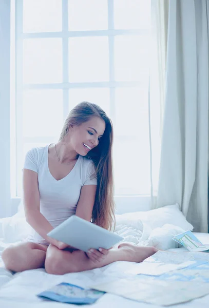 Ontspannen jonge vrouw zittend op bed met een kopje koffie en digitale tablet — Stockfoto