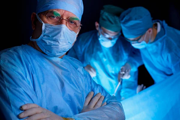 Gruppe af kirurger på arbejde i opererer teater tonet i blåt. Medicinsk team udfører operation - Stock-foto