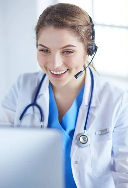 Médico con auriculares sentado detrás de un escritorio con portátil —  Fotos de Stock