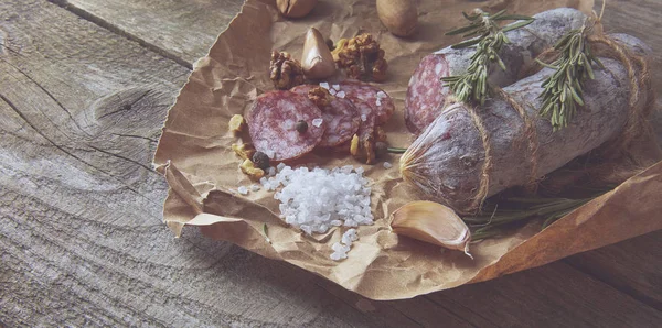 Franse salami en walnoten op ambachtelijke papier op houten achtergrond — Stockfoto