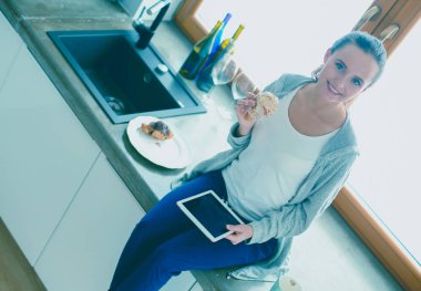 Mutfakta dijital tablet kullanan güzel genç bir kadın..