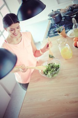 Gülümseyen genç kadın mutfakta taze salata karıştırıyor..