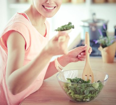 Gülümseyen genç kadın mutfakta taze salata karıştırıyor..