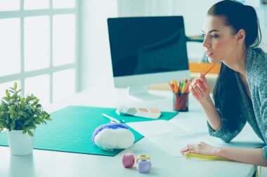 Moda tasarımcıları stüdyoda çalışıyor, masanın yanında duruyorlar.