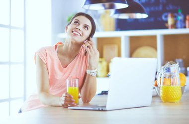 Mutfakta dizüstü bilgisayara benzeyen tariflerle gülümseyen genç bir kadın. Gıda blogcusu kavramı