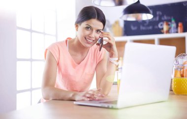 Mutfakta dizüstü bilgisayara benzeyen tariflerle gülümseyen genç bir kadın. Gıda blogcusu kavramı