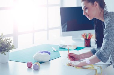 Moda tasarımcıları stüdyoda çalışıyor, masanın yanında duruyorlar.