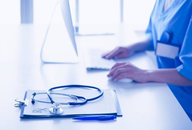 Kadın doktor masada oturuyor ve hastanede dizüstü bilgisayarla çalışıyor.