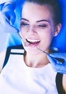 Dişçi muayenehanesinde diş muayenesi yapan ağzı açık genç bir kadın hasta..