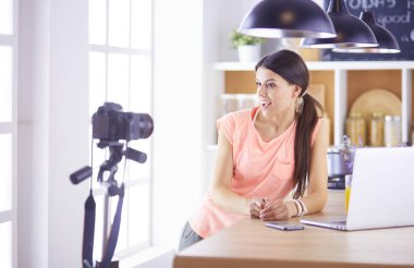 Mutfakta dizüstü bilgisayara benzeyen tariflerle gülümseyen genç bir kadın. Gıda blogcusu kavramı