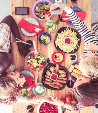 Ahşap masada otururken birlikte yemek yiyen bir grup insanın üst düzey görüntüsü. Masada yemek var. İnsanlar fast food yiyor..