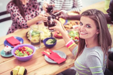 Ahşap masada otururken birlikte yemek yiyen bir grup insanın üst düzey görüntüsü. Masada yemek var. İnsanlar fast food yiyor. Bir kızın portresi.