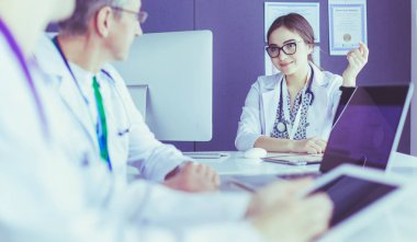 Ciddi bir tıbbi ekip parlak bir ofiste dizüstü bilgisayar kullanıyor.