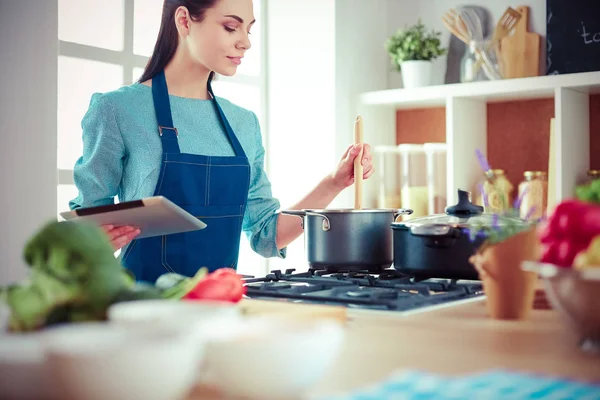 Mujer joven usando una tableta para cocinar en su cocina — Foto de Stock