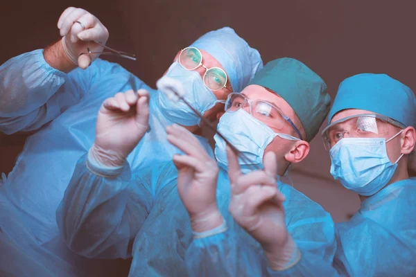 Grupo de cirurgiões no trabalho em sala de operações tonificada em azul. Equipe médica realizando operação — Fotografia de Stock