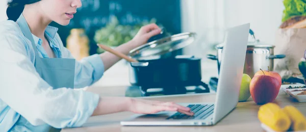 Young Woman in kitchen with laptop computer looking recipes, smiling. Food blogger concept — Stock Photo, Image