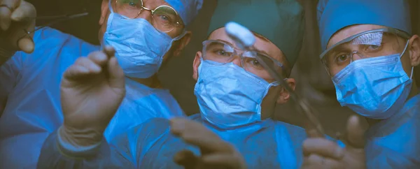 Grupo de cirurgiões no trabalho em sala de operações tonificada em azul. Equipe médica realizando operação — Fotografia de Stock