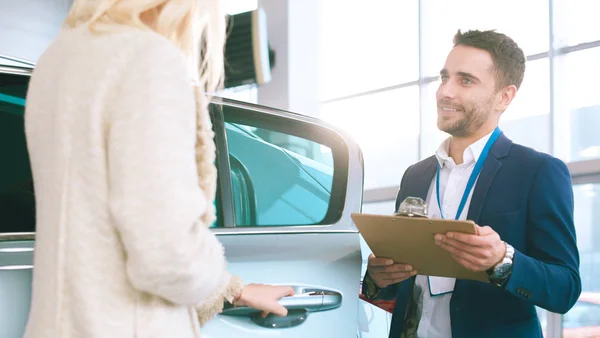 Hermosa mujer joven está hablando con el trabajador de concesionario de automóviles guapo al elegir un coche en concesionario — Foto de Stock