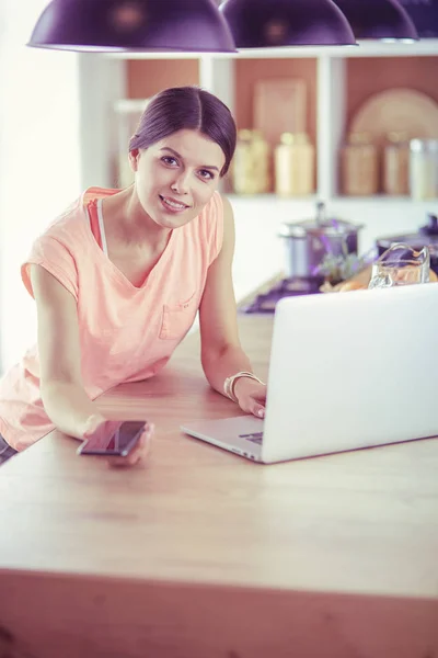 Vacker kvinna på telefon med bärbar dator hemma i köket — Stockfoto