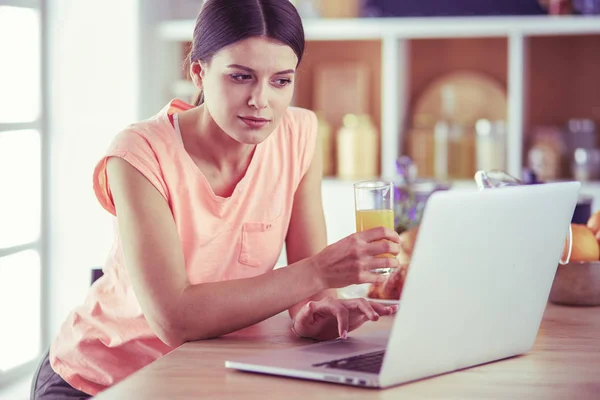 Ung kvinna i köket med bärbar dator ser recept, leende. Begreppet livsmedelsbloggare — Stockfoto