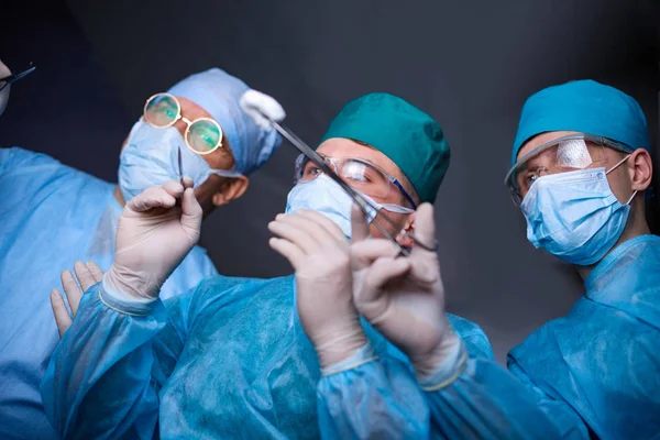 Grupo de cirurgiões no trabalho em sala de operações tonificada em azul. Equipe médica realizando operação — Fotografia de Stock