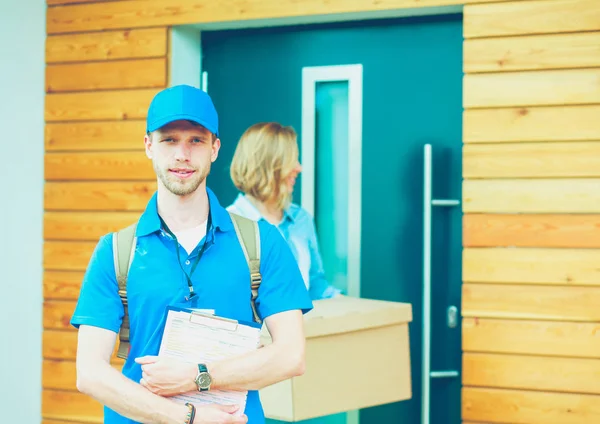 Repartidor sonriente con uniforme azul que entrega la caja de paquetes al destinatario: concepto de servicio de mensajería. Repartidor sonriente en uniforme azul — Foto de Stock