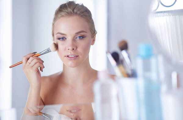 A picture of a young woman applying face powder in the bathroom