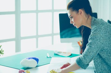 Moda tasarımcıları stüdyoda çalışıyor, masanın yanında duruyorlar.