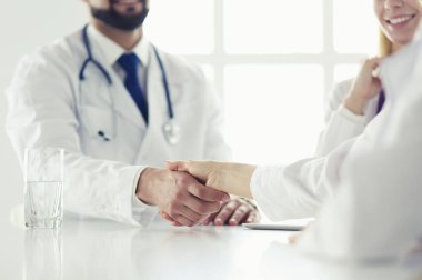 Doktor ofiste erkek bir hastayla el sıkışıyor.