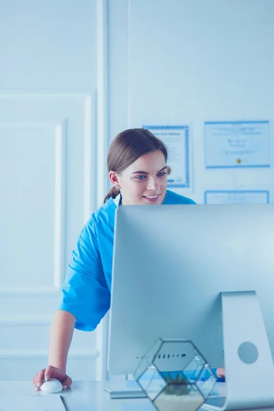 Portrait of female physician filling up medical form while standing near reception desk at clinic or emergency hospital