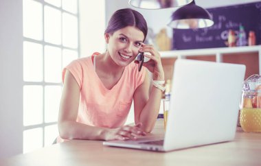 Mutfakta dizüstü bilgisayara benzeyen tariflerle gülümseyen genç bir kadın. Gıda blogcusu kavramı