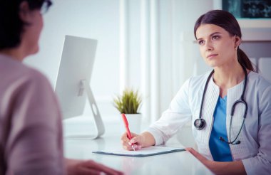 Doktor ve hasta hastane danışma odasında tıbbi sorunları tartışıyorlar. Doktor hasta formunu dolduruyor.